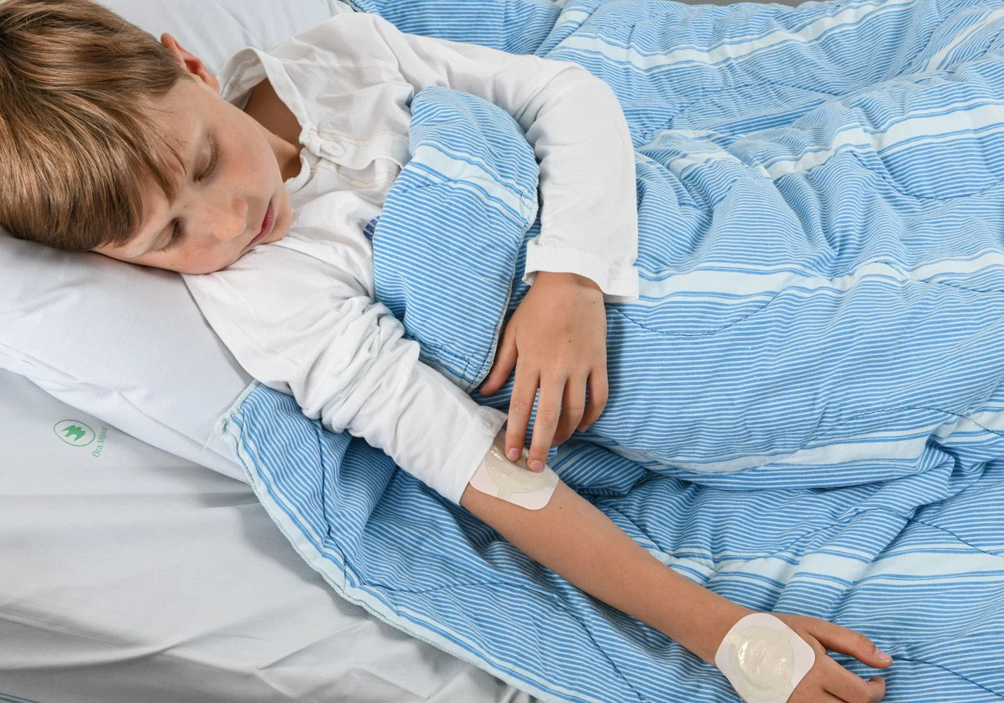 Pojke i en sjukhussäng. Bedövningsplåster på handryggen och i armvecket.