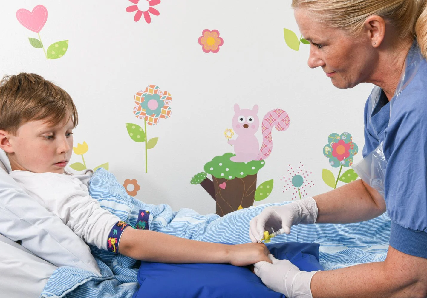 En pojke ligger i en sjukhussäng. En sjuksköterska sätter in en plastslang på pojkens handrygg.