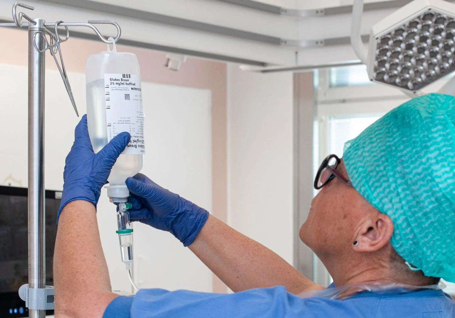 Sjuksköterska hänger upp ett dropp på en droppställning.
