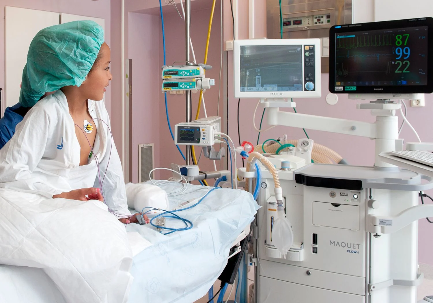 Flicka sitter på ett operationsbord och tittar på en övervakningsskärm.