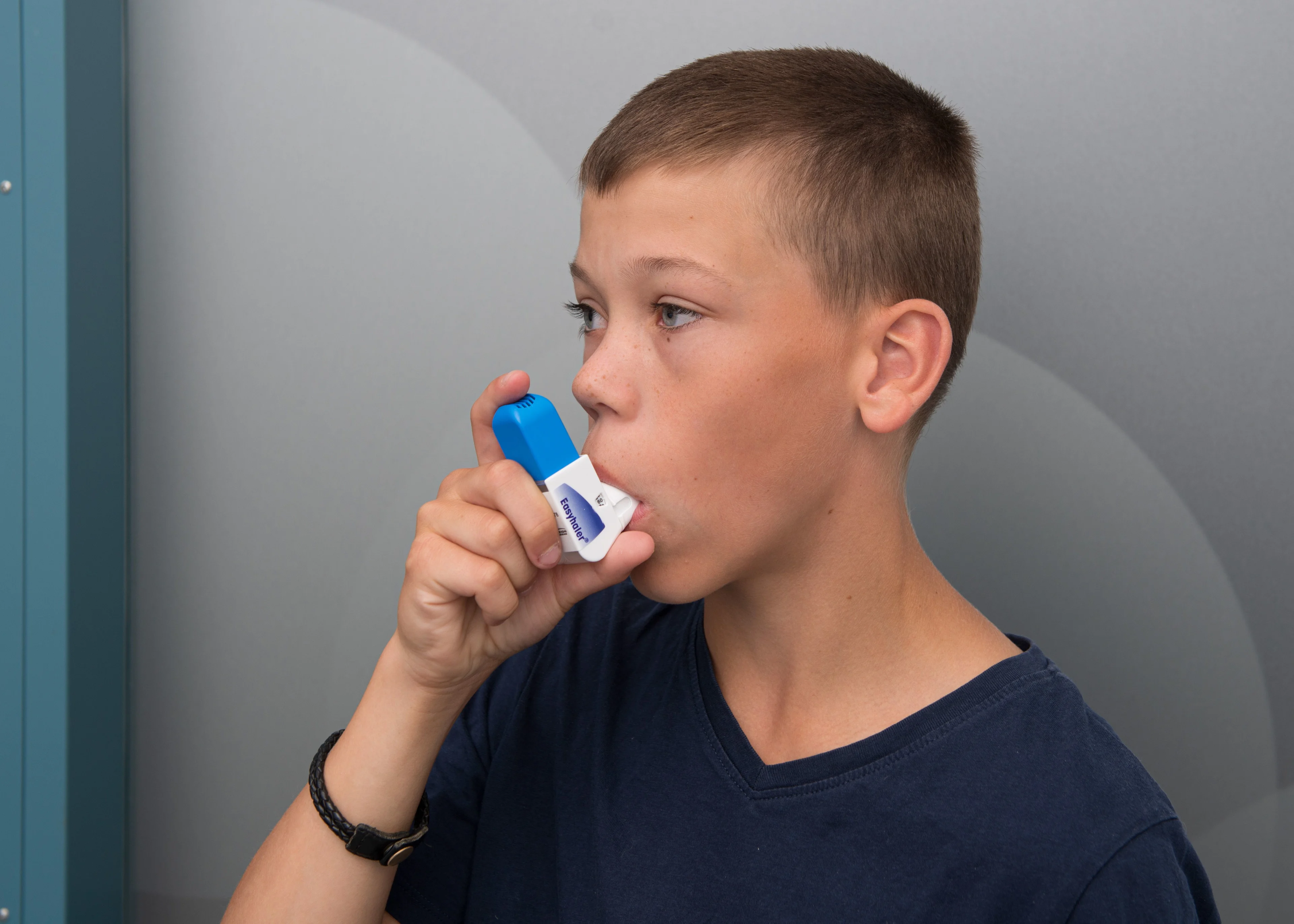 Pojke i grå tröja andas in medicin med en inhalator.