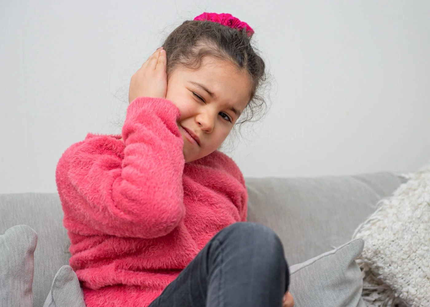 En flicka i rosa tröja och mörkt hår håller sig för örat.