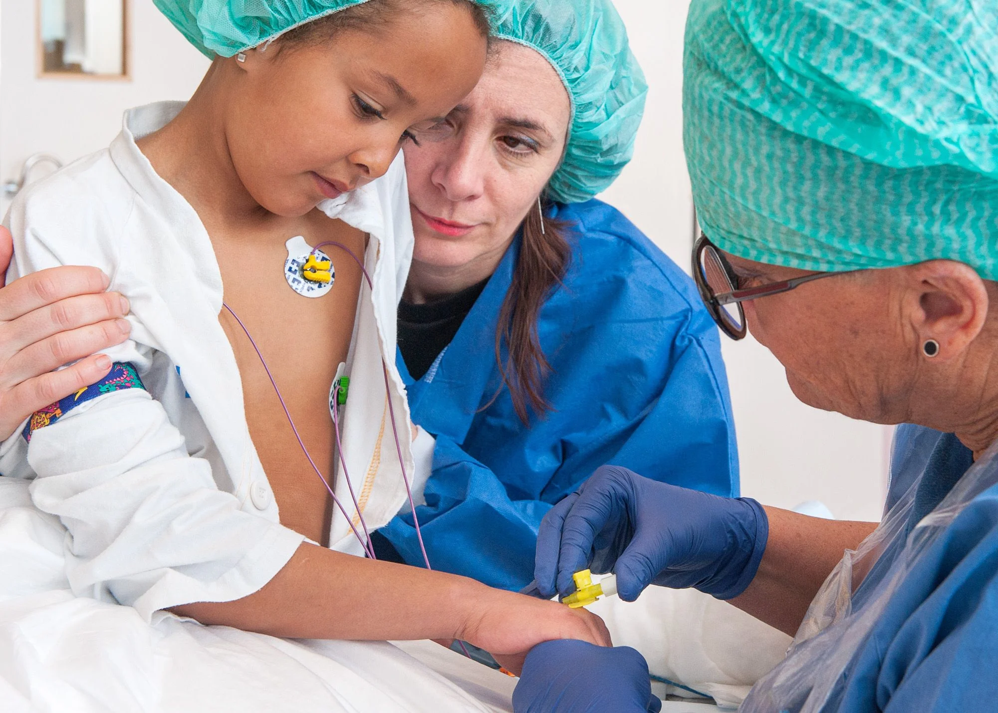 Sjuksköterska sticker en flicka i handen. Mamma håller om flickan.