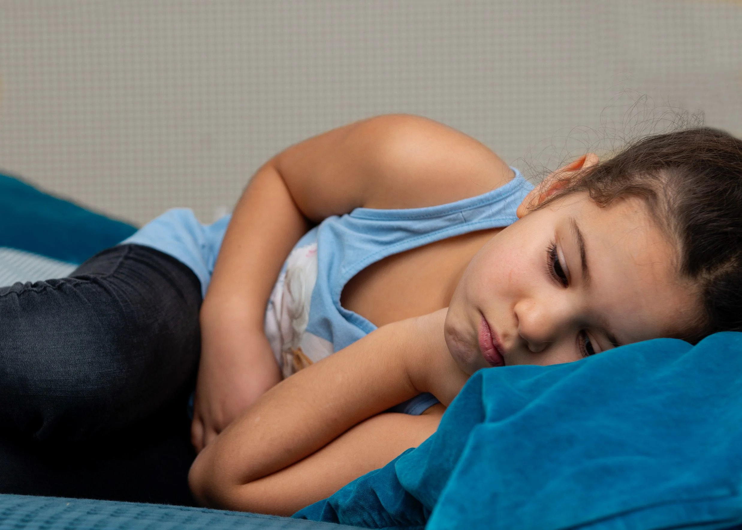 Flicka i ljusblått linne ligger ner. Håller sig för magen. Ser ut att ha ont i magen.