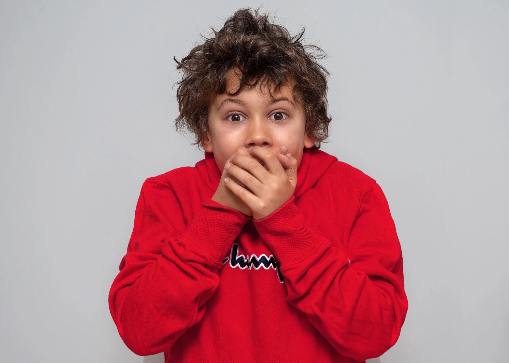 Pojke i röd hoodie håller händerna framför munnen.